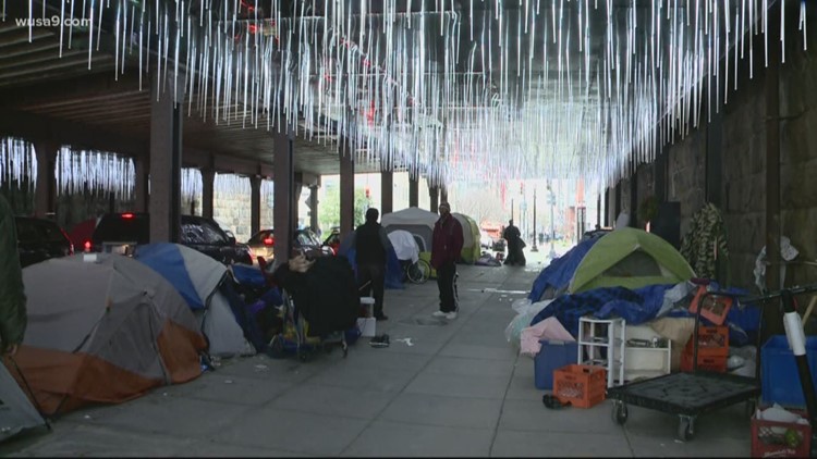 Railway underpass with fancy hanging light installation, populated by a sizable homeless encampment.